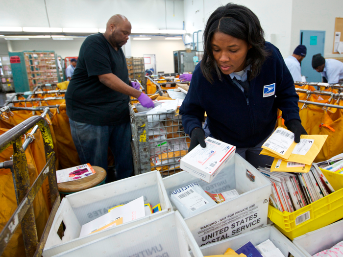 Workers sorting packages and mail at a United States Postal Service facility.