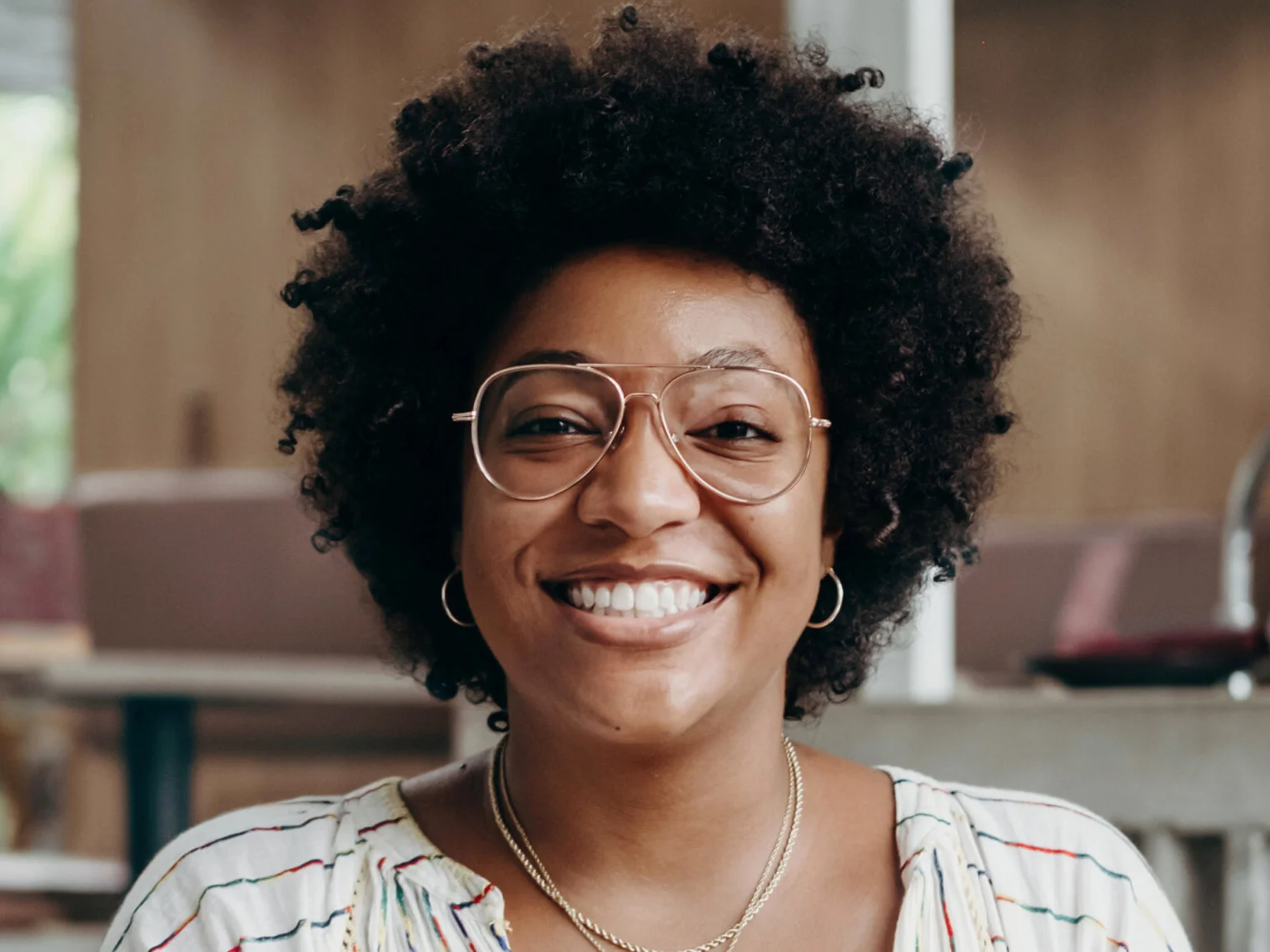 Smiling woman with glasses and hoop earrings in a casual indoor setting.